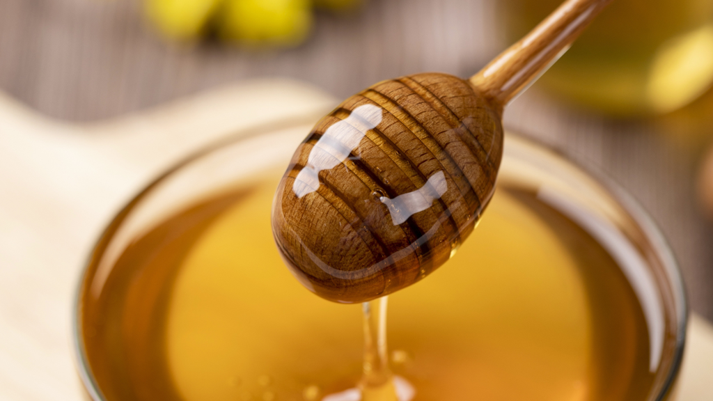 Wooden honey spoon being held over honey pot