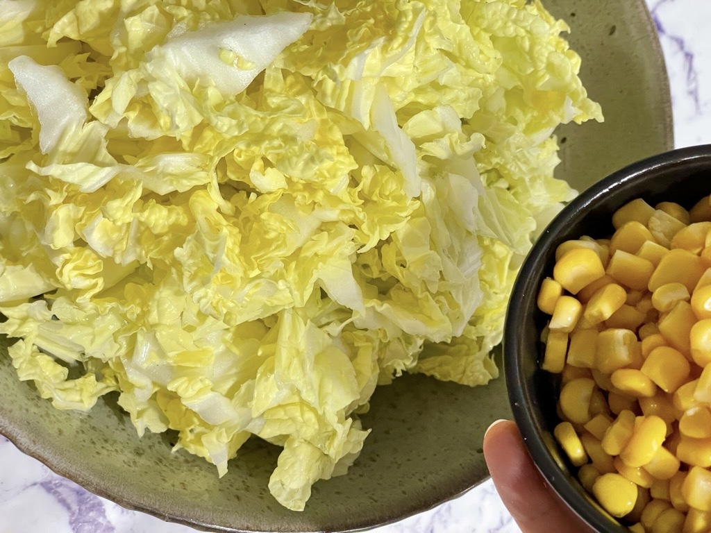 Bowl of chopped salad under hand holding bowl of corn kernels