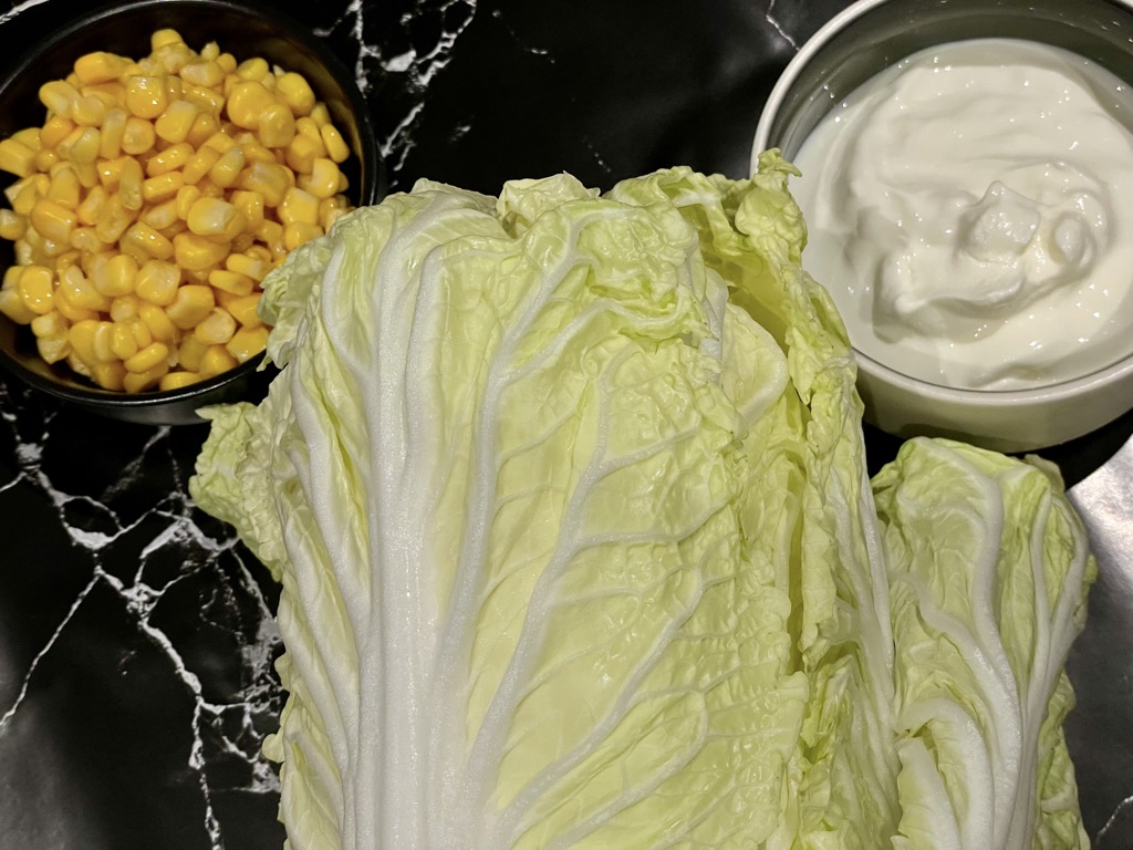 Black bench wit bowl of yoghurt, bowl of corn kernels and whole head of Chinese cabbage