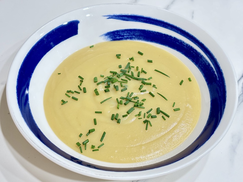 White soup bowl filled with creamy potato soup topped with chives in white and blue soup bowl