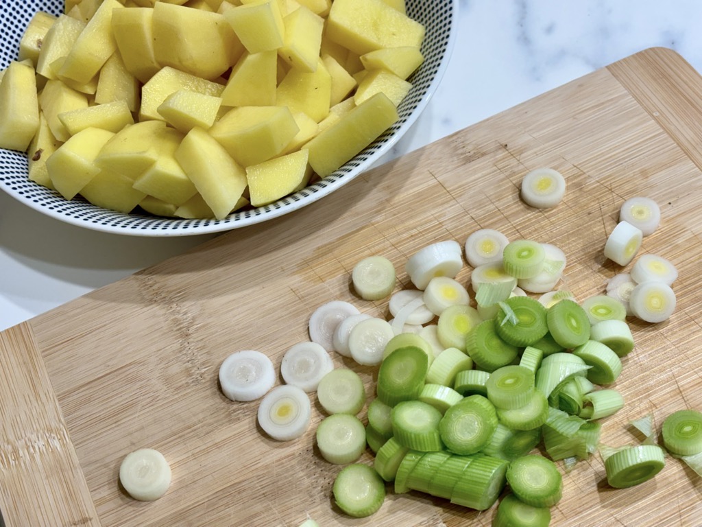 Bowl of chopped potatoes and wooden board of sliced leek