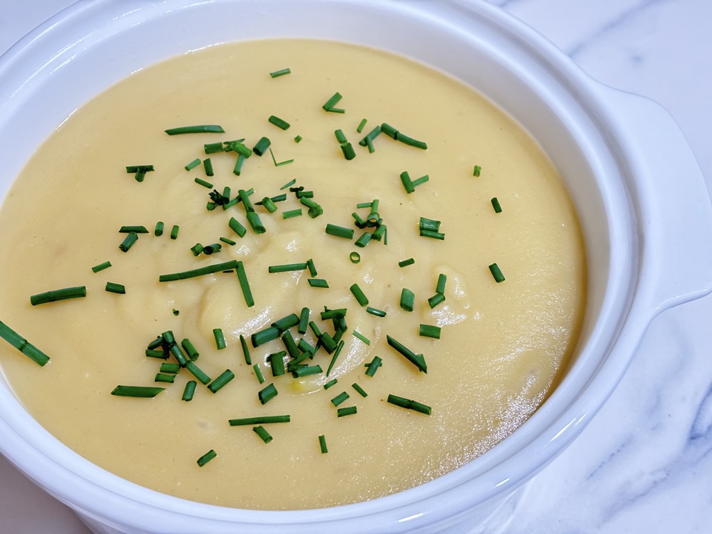 White soup bowl filled with creamy potato soup topped with chives