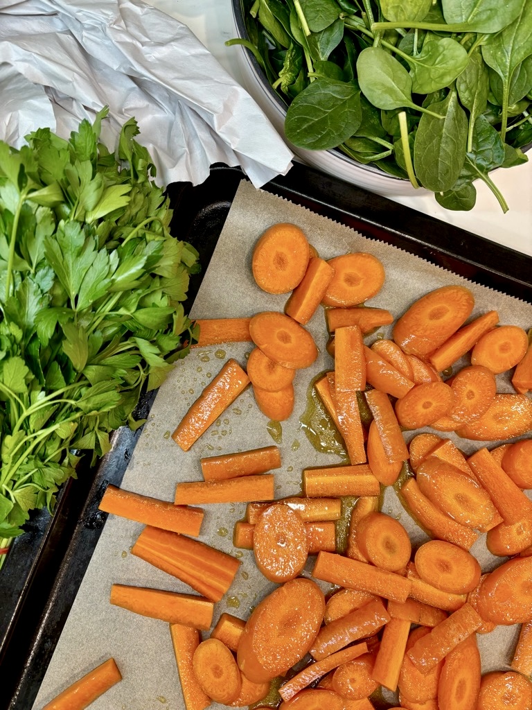 Bowl of baby spinach, bunch of parsley and sliced carrots on baking tray