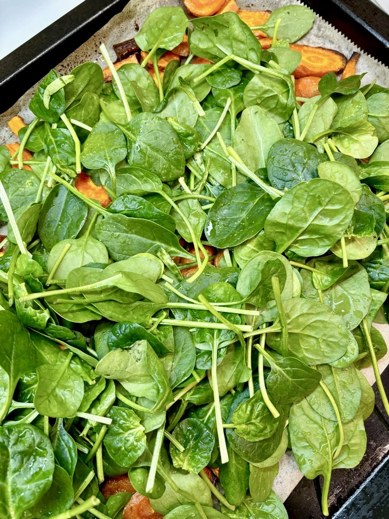 Baking tray filled with carrots, topped with lots of baby spinach