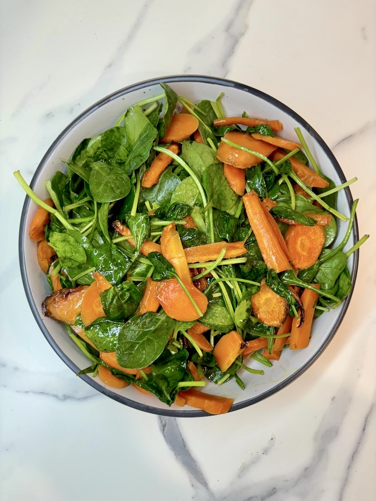 White bowl on marble surface, filled with roasted carrots and spinach