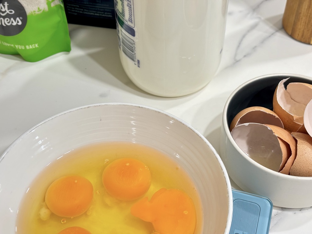 Eggs in bowl next to bowl of shells and bottle of milk