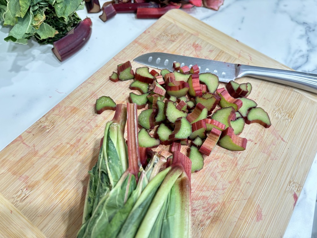 Freshly cut pieces of rhubarb on wooden cutting board with silver knife