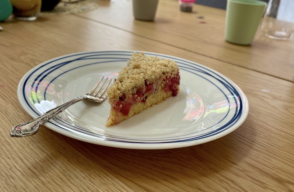 Slice of rhubarb streusel cake on plate with fork, placed on wooden table