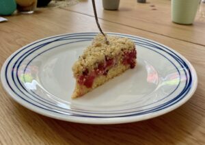 Slice of rhubarb streusel cake on plate with fork stuck into it, placed on wooden table