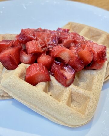 Three waffles on white plate, topped with stewed rhubarb