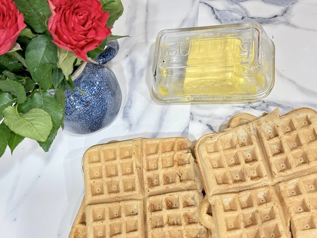 Large waffle squares next to blue vase with pink roses and glass butter dish