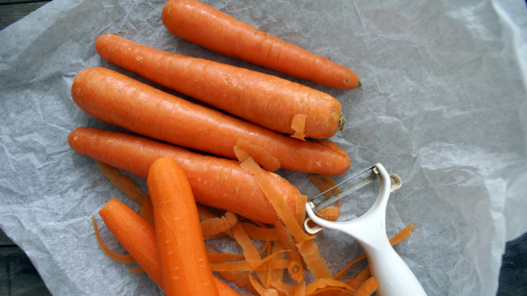 carrots and white peeler on white parchment paper