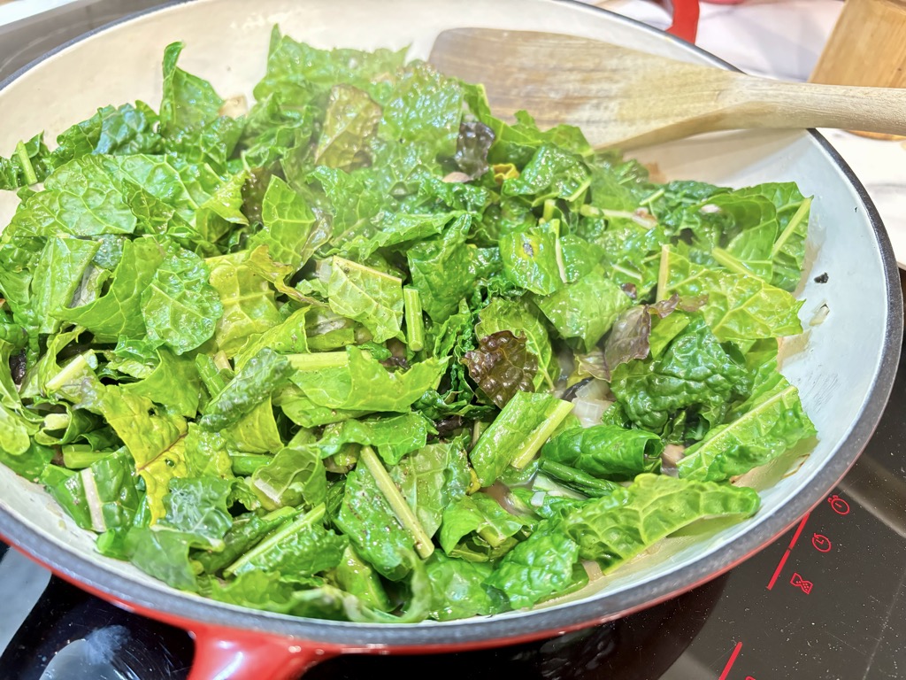 Red pan filled with chopped kale leaves placed on hot stove