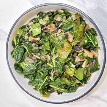 White dish filled with cooked kale and mushrooms on marble surface