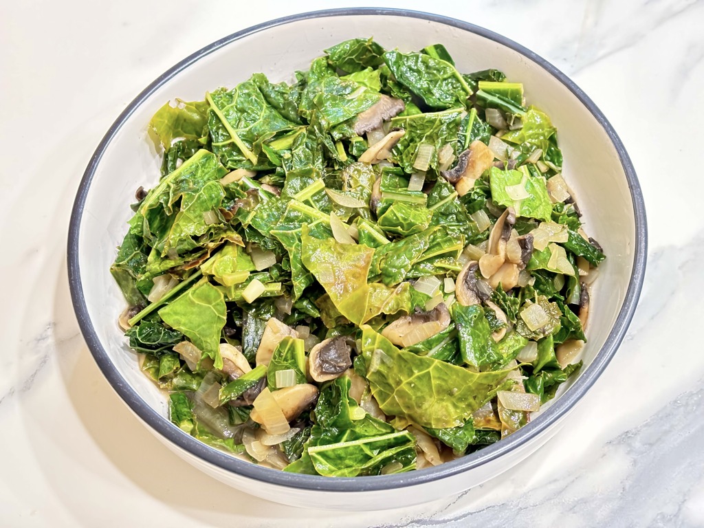 White dish filled with cooked kale and mushrooms on marble surface