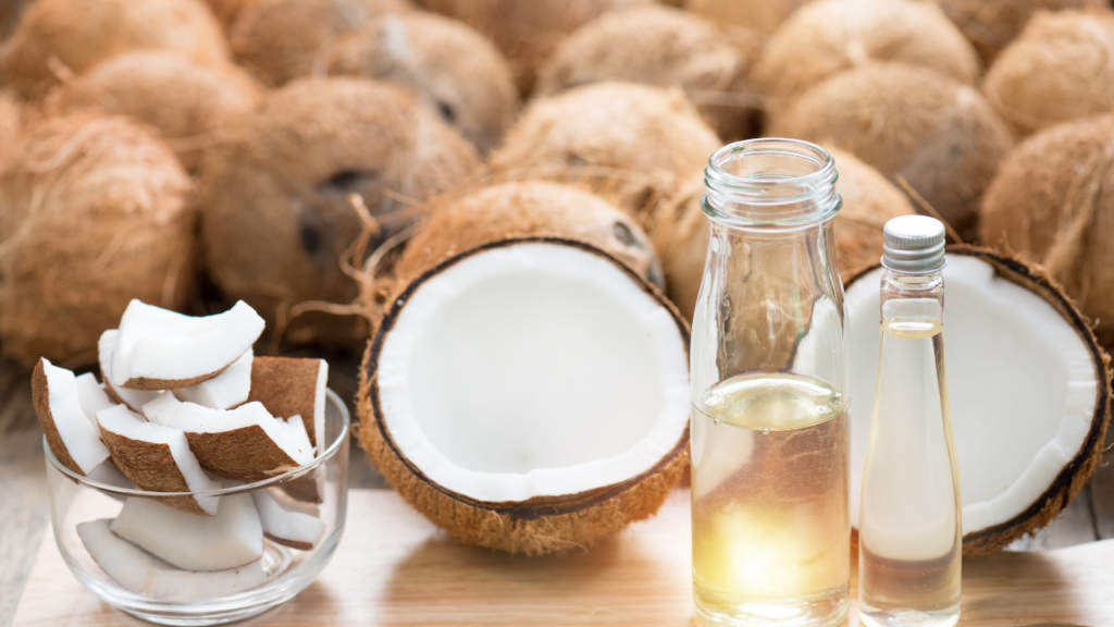 Cut pieces and two halves of coconut, together with two bottles of coconut oil, standing in front or many coconuts in background