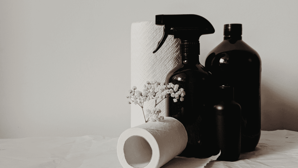 Kitchen roll and cleaning sprays in dark bottles on white background