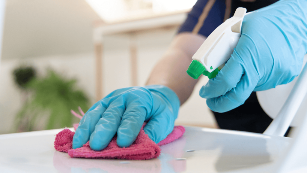 Hands in blue rubber gloves cleaning kitchen bench with pink cloth