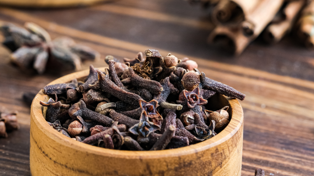 small wooden bowl filled with cloves in front of cinnamon sticks