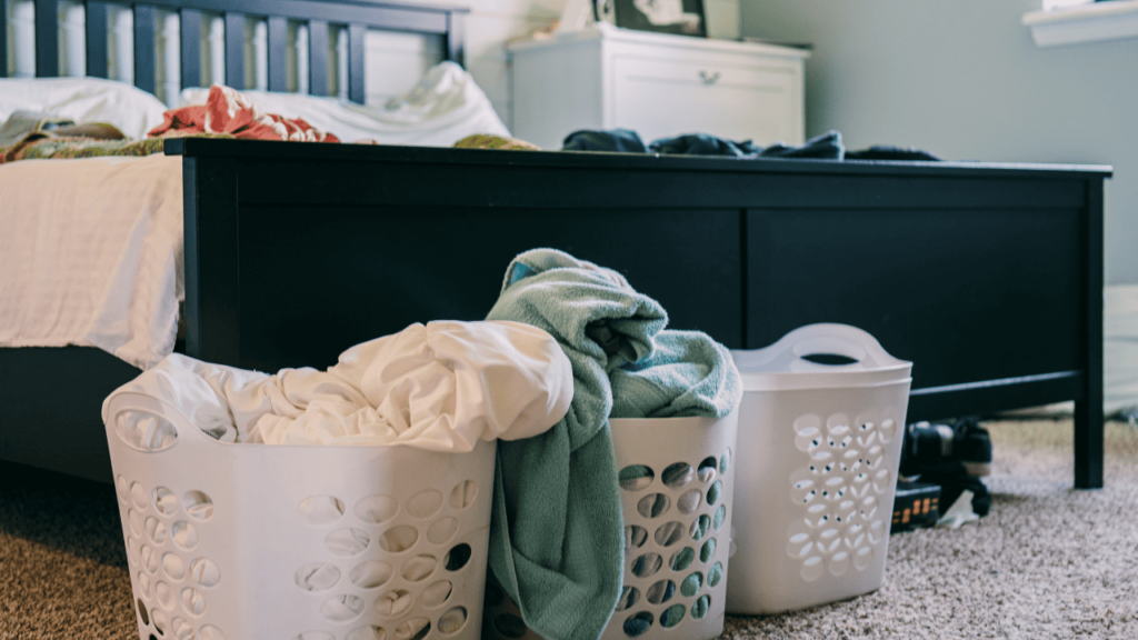 Three white laundry baskets standing in front of black bed