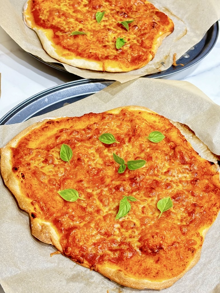 two no yeast sourdough margarita pizzas on baking sheets topped with basil