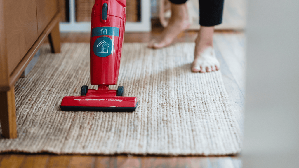 Red vacuum cleaner being run over cream coloured rug