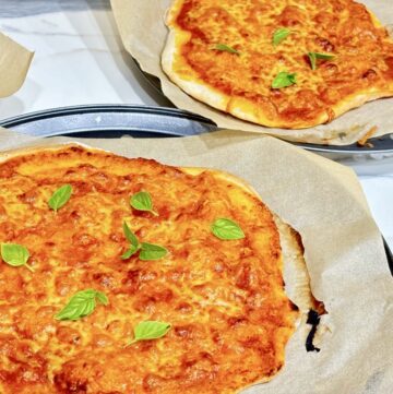 two margarita pizzas on baking sheets topped with basil