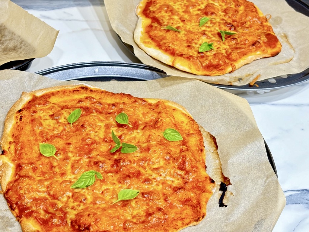 two margarita pizzas on baking sheets topped with basil