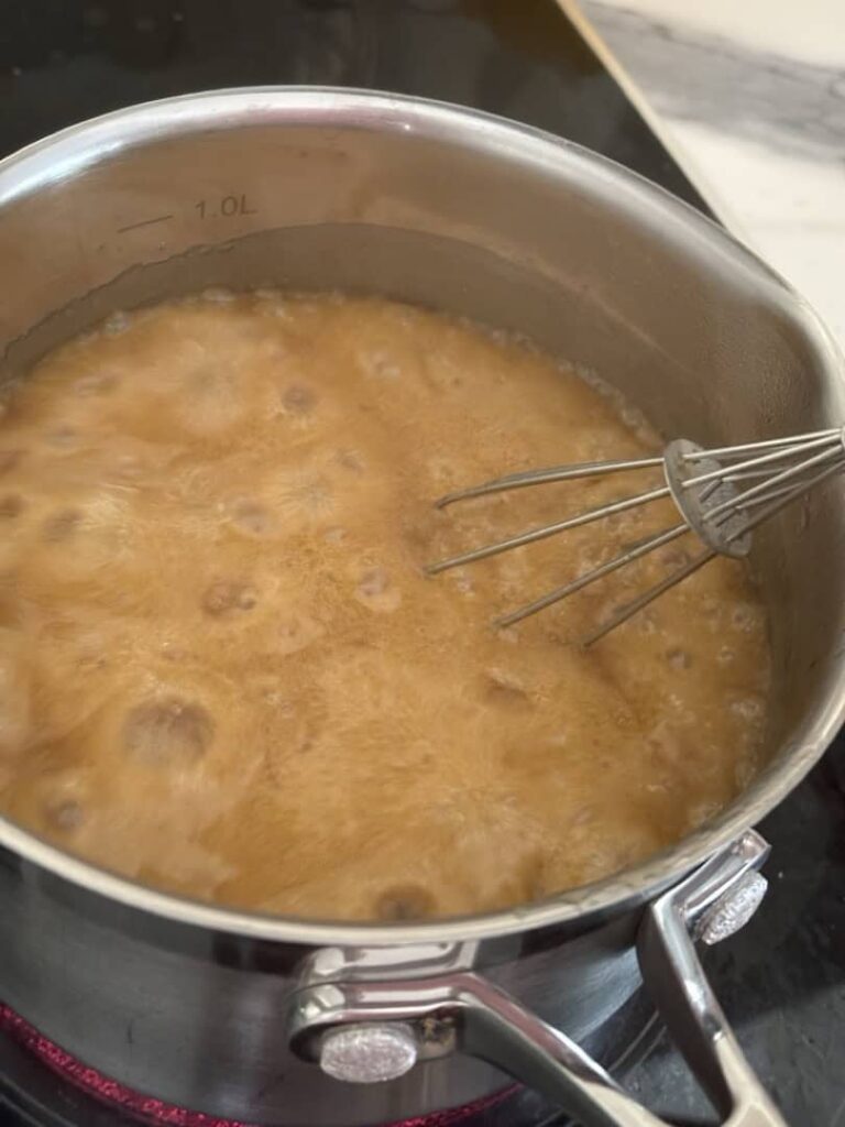 Bubbly caramel sauce in silver pot with silver whisk