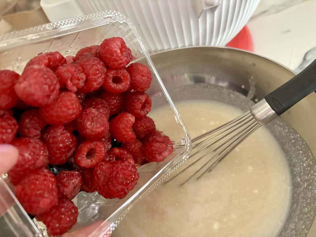 punnet of raspberries being tipped into metal bowl filled with coconut milk