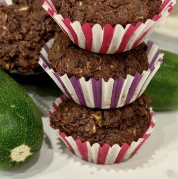 Stack of 3 chocolate zucchini muffins next to fresh zucchini