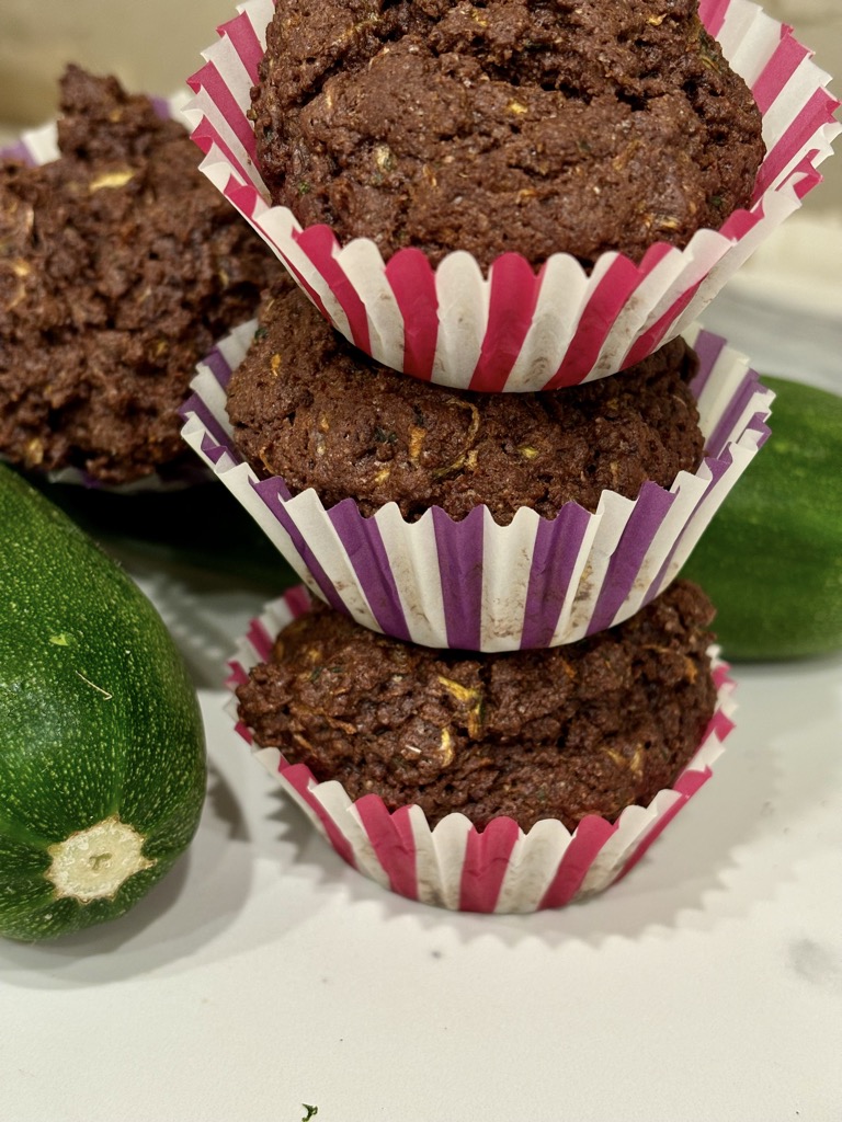 Stack of 3 chocolate zucchini muffins next to fresh zucchini