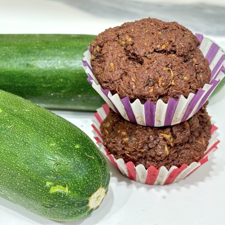 Two dark chocolate zucchini muffins next to two zucchinis