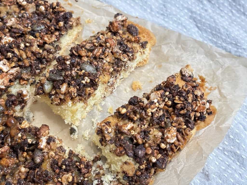 Two slices of sweet and salty granola bars on parchment paper next to full tray of granola bar