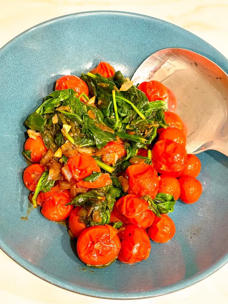 tomato and spinach saute in blue serving bowl with silver spoon