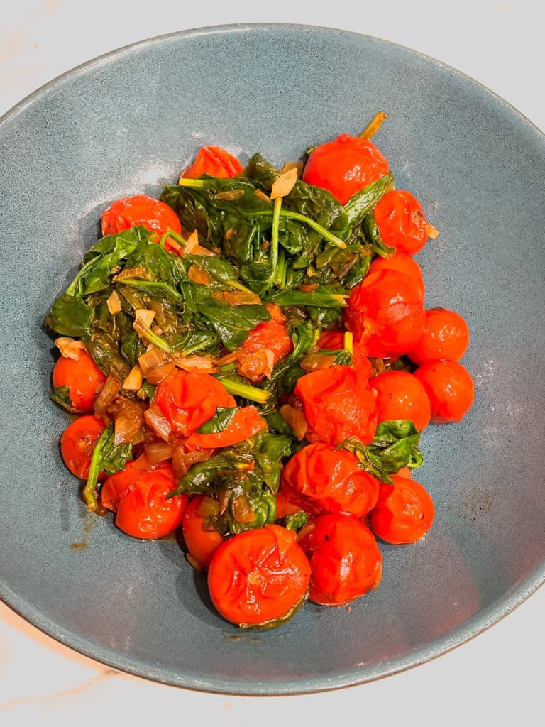 top down shot of tomato and spinach saute in blue serving bowl