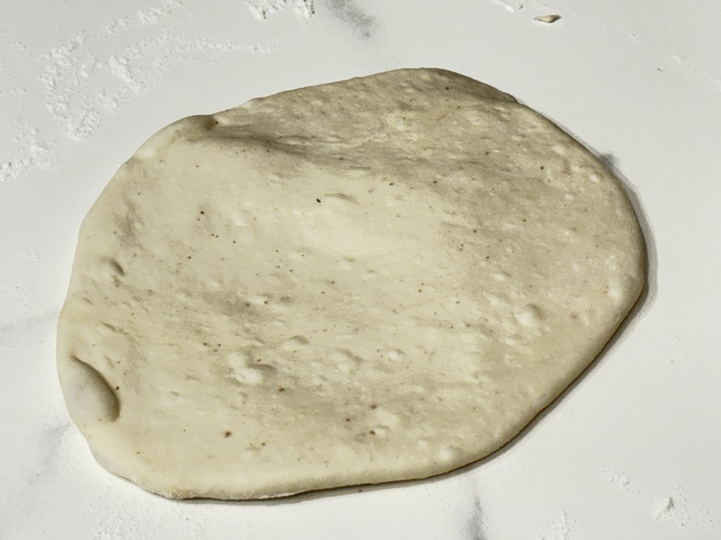 single piece of rolled out pizza dough on floured surface