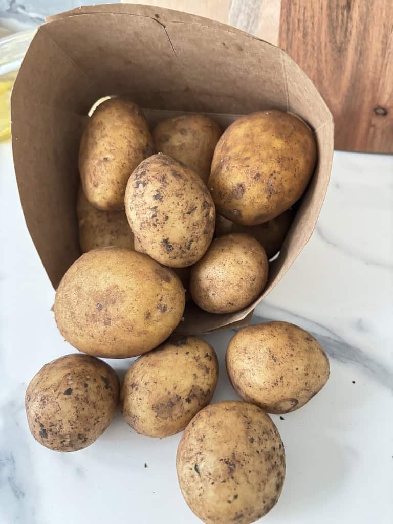 Paper carton of potatoes tipped on its side with potatoes tumbling out