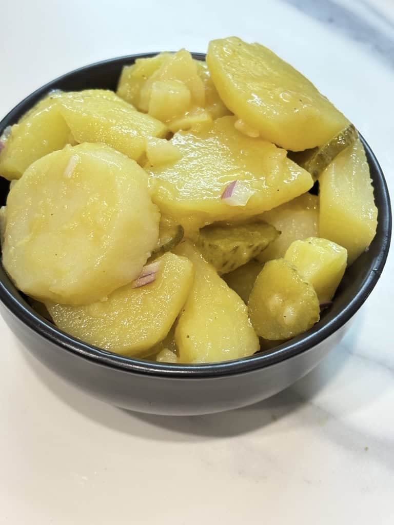 Small black bowl of potato salad standing on kitchen counter