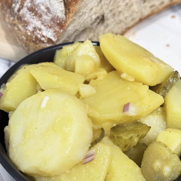 Small black bowl of potato salad standing on kitchen counter in front of rustic bread loaf