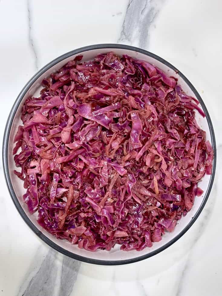 Braised red cabbage and apple in white serving bowl with black rim