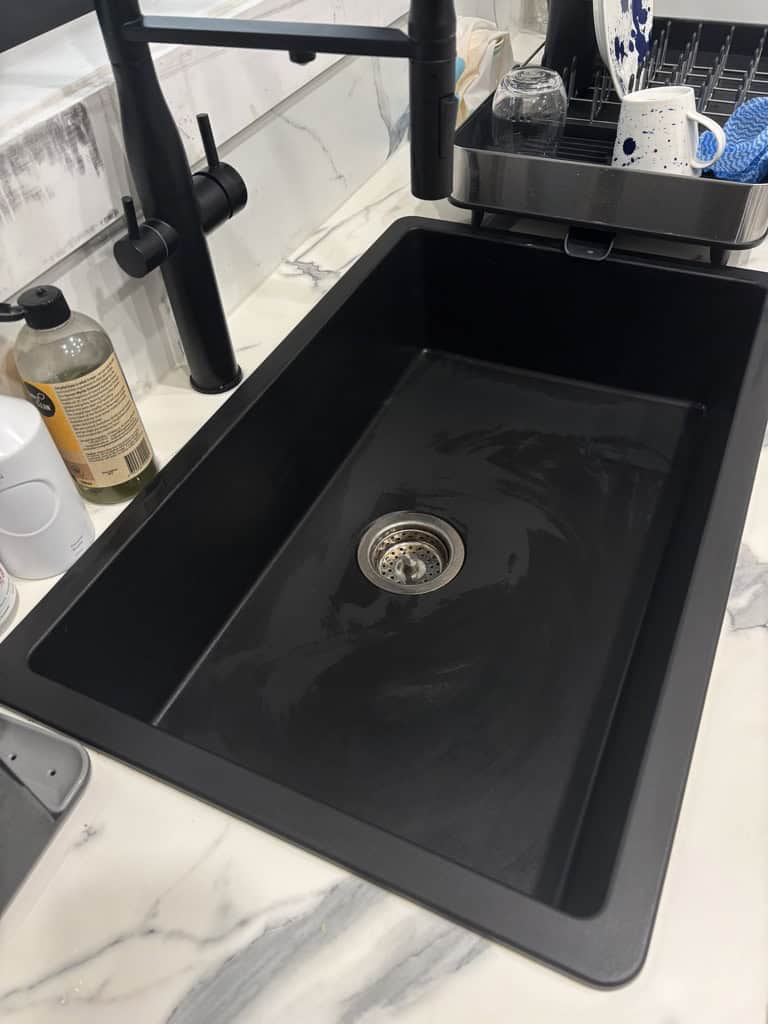 Cleaned and dried black kitchen sink on marble bench with black tap above it