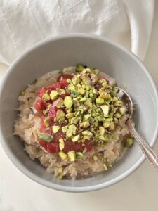 Rice Flakes Porridge in grey bowl with silver spoon, topped with rhubarb and chopped pistachios on white linen napkin