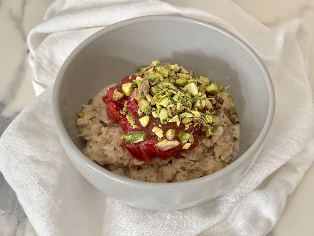 Rice Flakes Porridge topped with rhubarb and chopped pistachios on white linen napkin