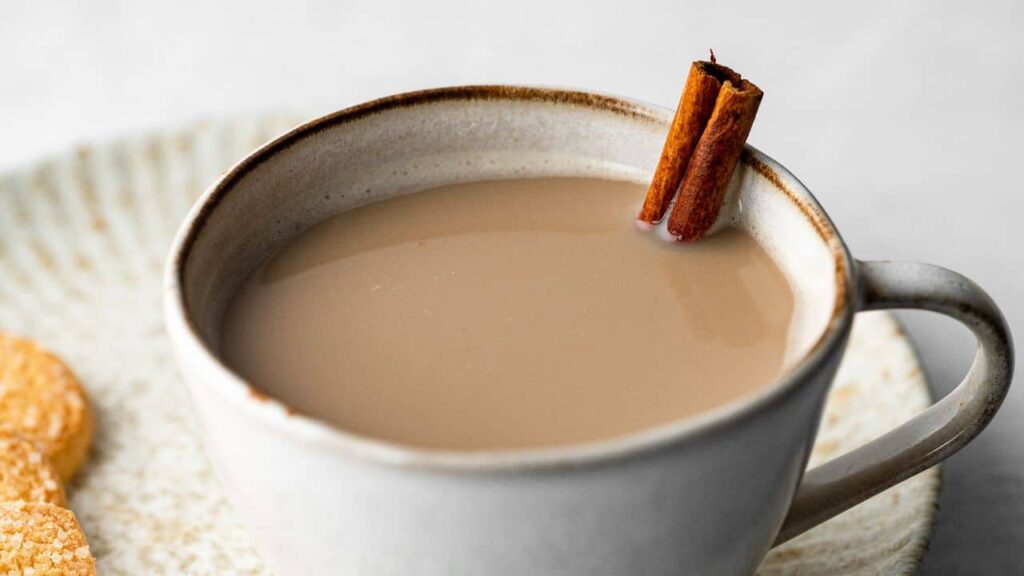 Light blue cup filled with chai latte and cinnamon stick sticking out on saucer with 3 biscuits