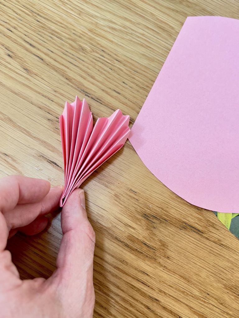 Women's hand pressing together edges of folded pink paper heart