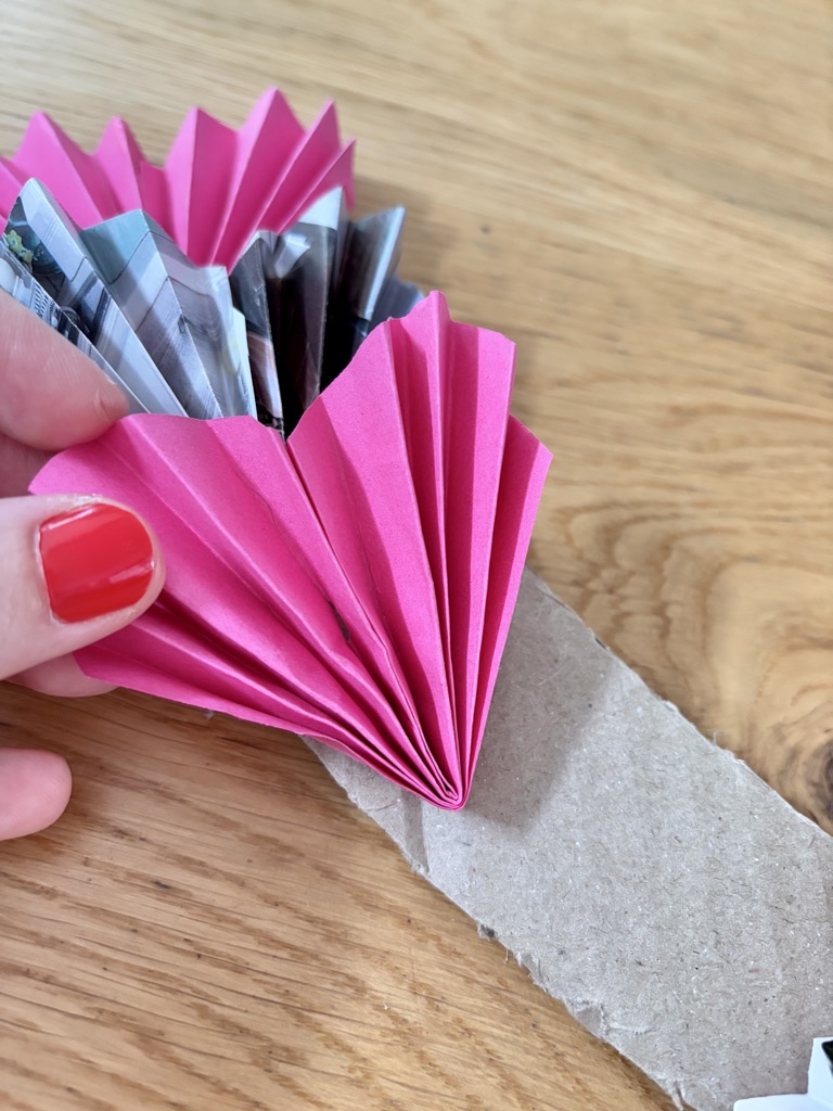 Hand sticking folded paper hearts onto cardboard wreath frame