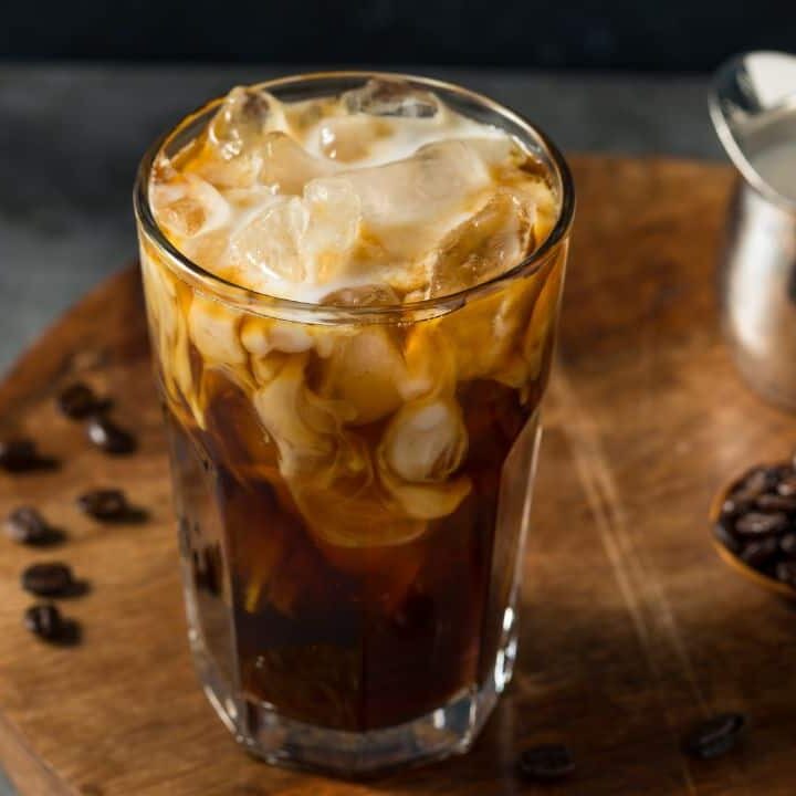 Iced coffee on wooden board with coffee beans and small silver jar of milk