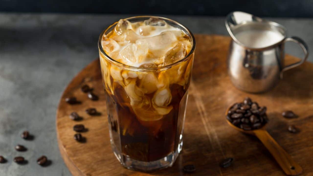 Iced coffee on wooden board with coffee beans and small silver jar of milk