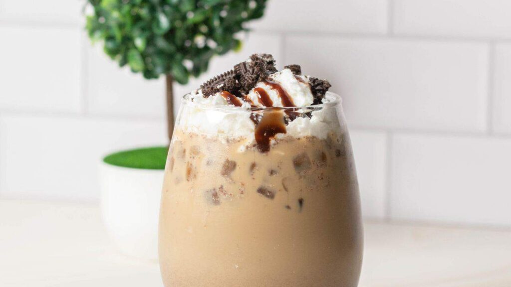 Iced coffee topped with cream and crushed up Oreos in tall glass